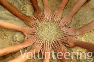 Image of different hands coming together in the sand symbolizing the power of volunteering.